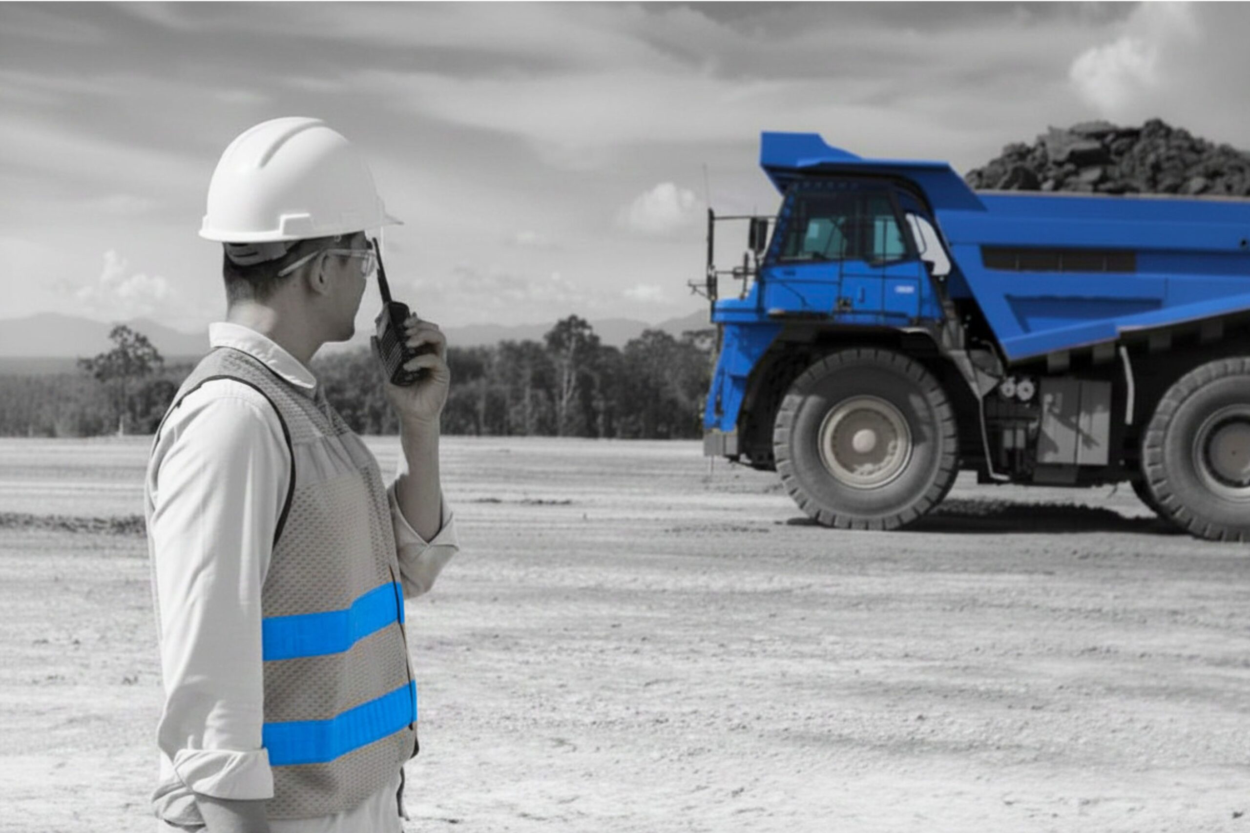 Mining supervisor with a two-way radio beside a haul truck at an Australian open pit mine